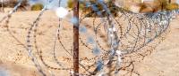 A barbed-wire fence in a desert with buildings in the background